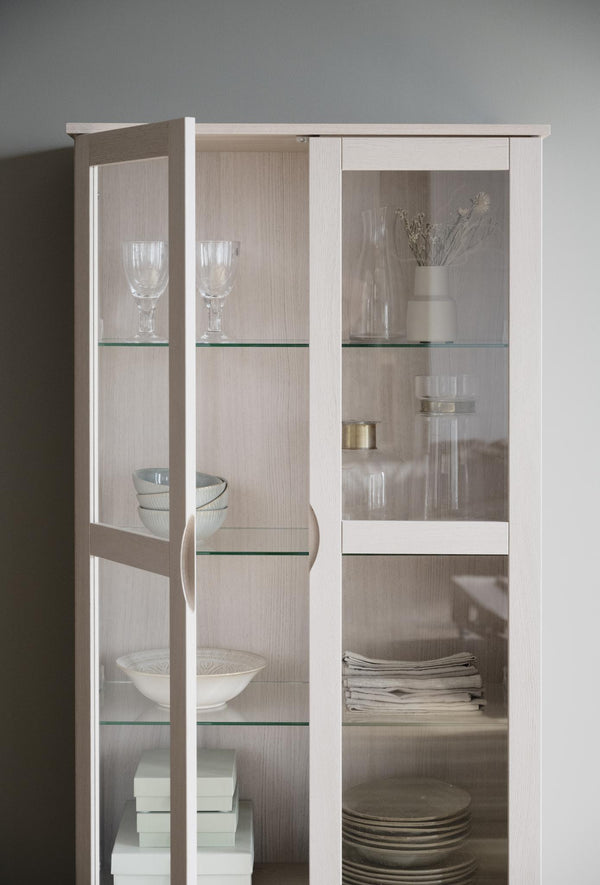 Vitrinskåp i vit med glashyllor och glasdörrar, inrett med glas, keramik och textilier