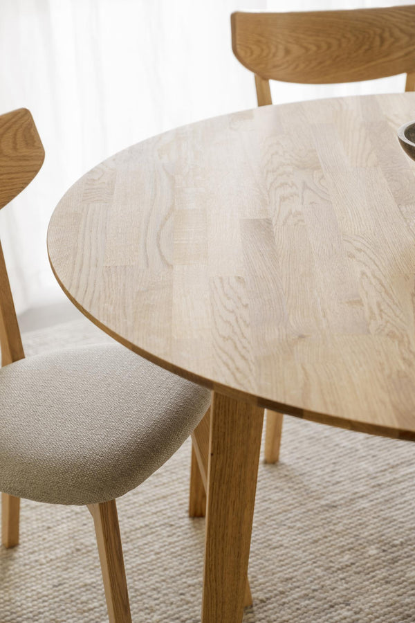 Runt matbord i ljust trä med synlig ådringsmönster och matchande stolar med beige stoppad sits