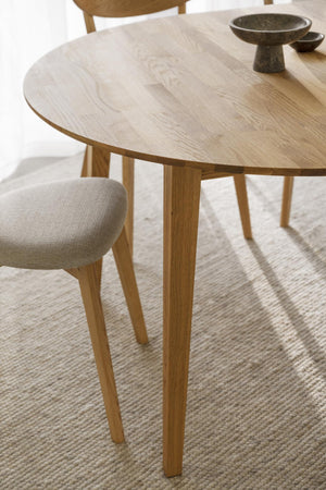 Runt matbord i ljust trä med tre ben och synlig träådring, med stol och skålar på bordet