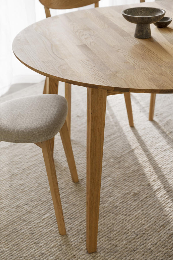 Runt matbord i ljust trä med tre ben och synlig träådring, med stol och skålar på bordet