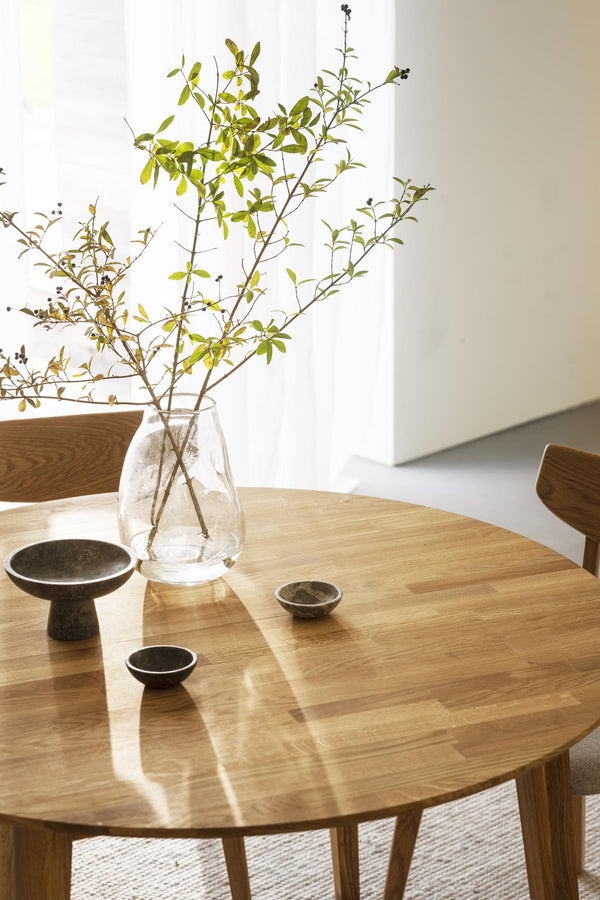 Runt matbord i ek med glasvas med grenar och keramikskålar i minimalistisk skandinavisk stil