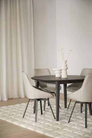 Rund matbord i mörkt trä med fyra beige stoppade stolar på ljus matta i minimalistisk matsal