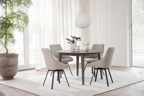 Matgrupp med runt grått bord och fyra beige stolar i ljus matsalsmiljö med vita gardiner