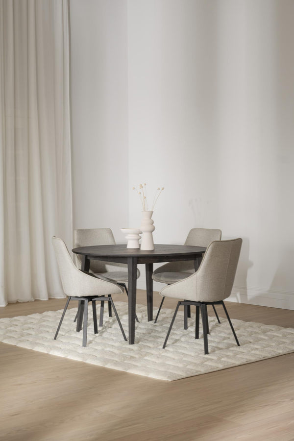 Runt matbord i mörkt trä med fyra beige stoppade stolar på ljus matta i minimalistisk matsal