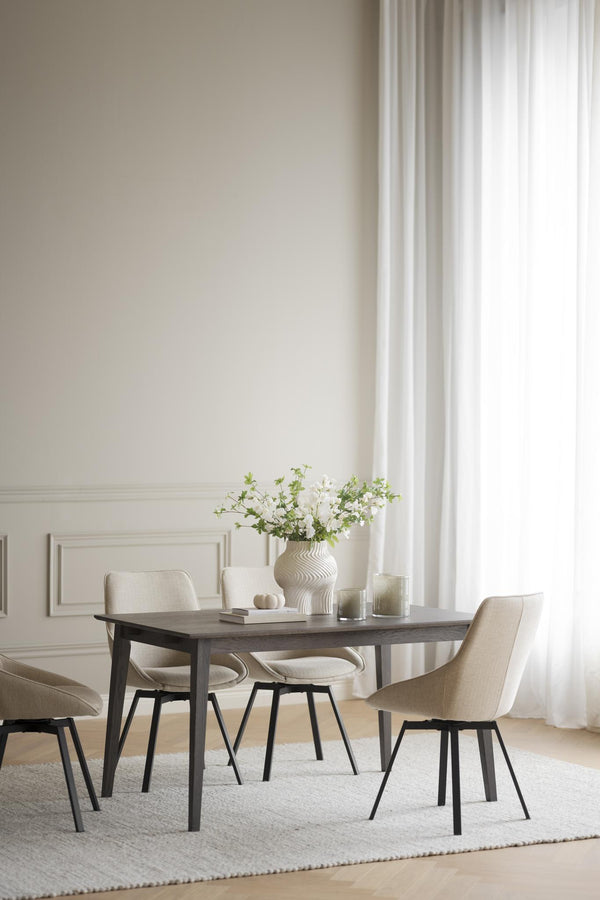 Matbord i mörkt trä med beige stolar och vit vas med blommor i ljust matrum med gardiner