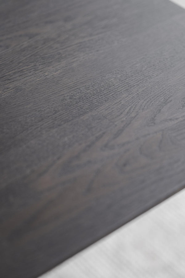 Närbild av mörkgrå träyta med synlig struktur och årringmönster, vit kant i nedre hörnet