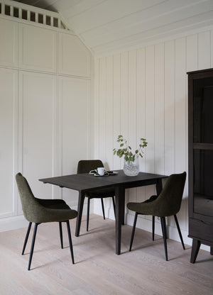 Svart matbord med fyra gröna stolar i skandinavisk design, stilleben med kopp och vas med eukalyptus