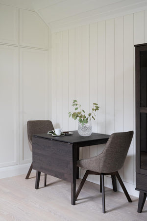 Matbord i mörkt trä med två grå stolar i modern skandinavisk stil mot vit panelvägg