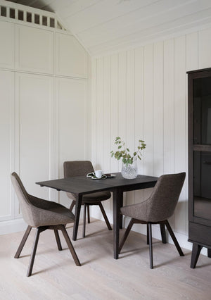 Matbord i mörkt trä med tre stolar i grå klädsel, vit pärlspont vägg och ljust trägolv
