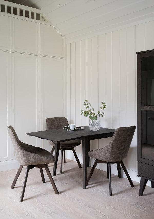 Matbord i mörkt trä med tre stolar i grå klädsel, vit pärlspont vägg och ljust trägolv
