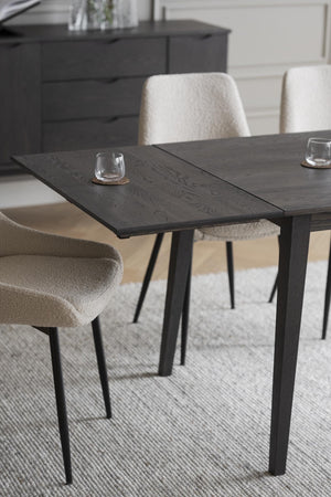 Svart matbord i trä med fyrkantiga ben och upphällda stolar i beige och vitt tyg