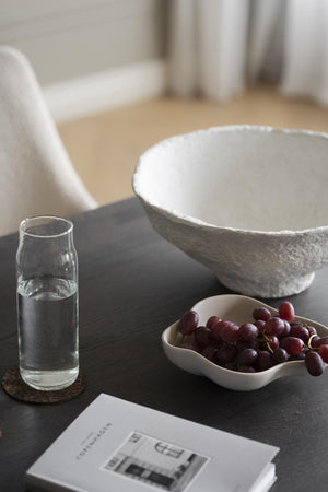 Stilren dekoration med stor keramikskål, vattenkaraff och druvor på mörkt träbord i minimalistisk inredning