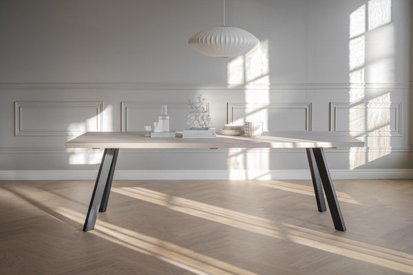 Matbord med ljus träskiva och svarta snedställda ben i modernt minimalistiskt rum med naturligt ljus