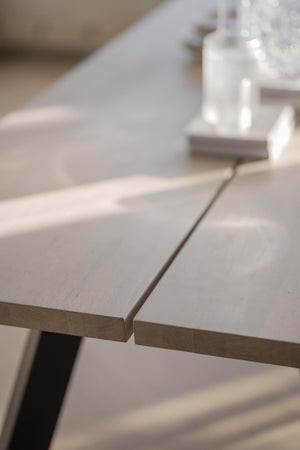 Närbild på ljust träbord med synlig fog mellan bordsskivor och svart metallben