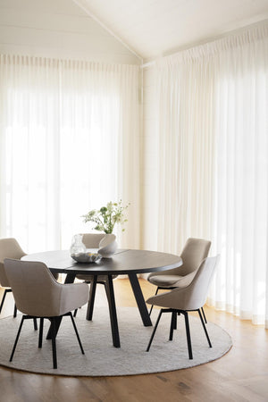 Matplats med runt bord, beige stolar och vita genomskinliga gardiner i ljust rum med trägolv