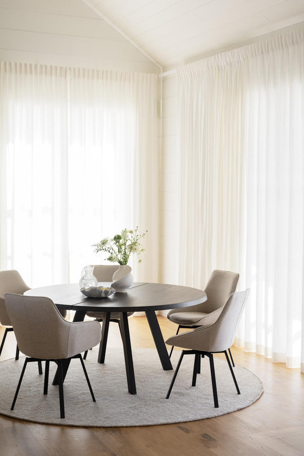 Matplats med runt bord, beige stolar och vita genomskinliga gardiner i ljust rum med trägolv