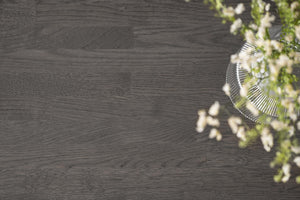 Mörkgrå trägolv med synlig trästruktur och dekorativ grön växt i hörnet