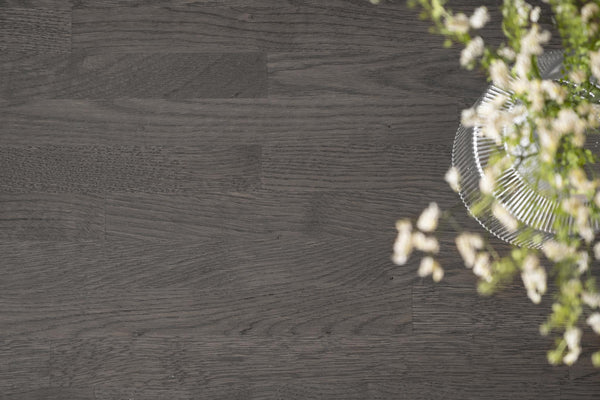 Mörkgrå trägolv med synlig trästruktur och dekorativ grön växt i hörnet