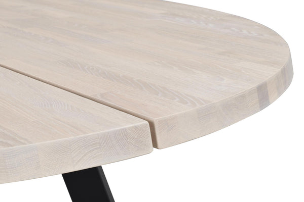 Runt matbord i ljust trä med träfibermönster och svart metallben, närbild av bordskanten