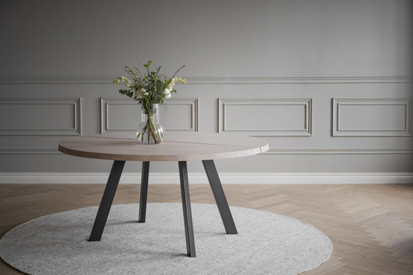 Runt matbord med träskiva och svarta metallben på ljus matta i elegant matsal med grå vägg