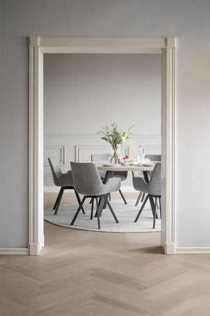 Matgrupp med grå stolar och runt bord i ljus matsal med vit väggpanel och parkettgolv i fiskbensmönster