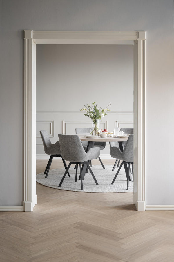 Matgrupp med grå stolar och runt bord i ljus matsal med vit väggpanel och parkettgolv i fiskbensmönster