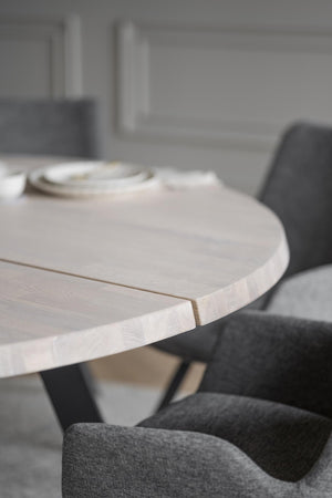 Runt matbord i ljust trä med grå stoppade stolar i modern skandinavisk matsal