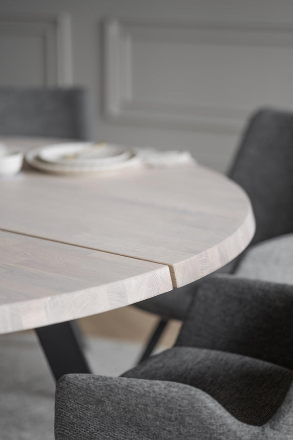 Runt matbord i ljust trä med grå stoppade stolar i modern skandinavisk matsal