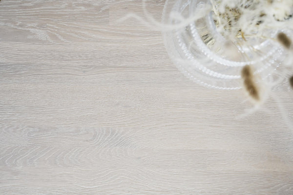 Ljust trägolv i ek med glasvas innehållande torkade blommor