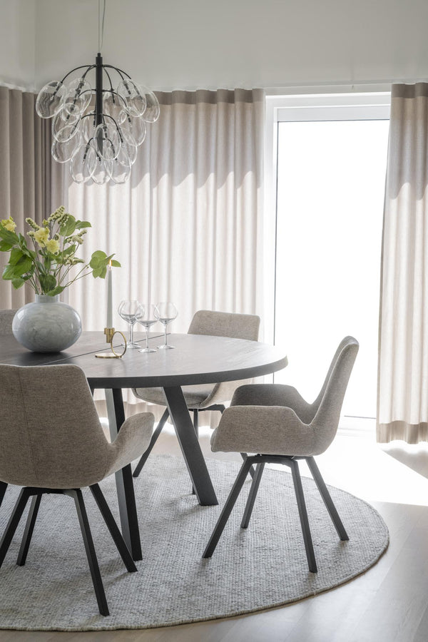 Matgrupp med runt grått bord och fyra grå stolar under glaslampa i ljus matsal med beiga gardiner