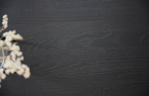 Mörk träbakgrund med suddig vit torkad blomma i vänster hörn, naturlig textur för produktfotografi