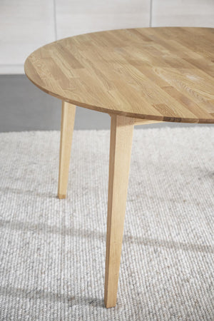 Runt soffbord i ljust trä med tre ben på ljusgrå matta i skandinavisk stil