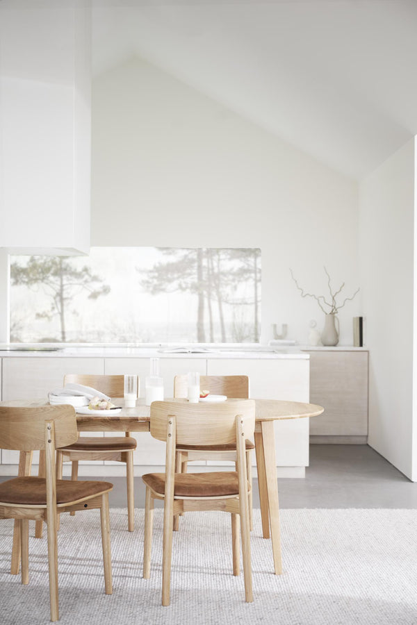 Ljus matplats med runt matbord i trä och stolar med bruna sittdynor i skandinavisk stil