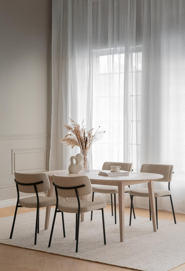 Rund matbord i ljust trä med beige stoppade stolar i minimalistisk matsal med vita gardiner
