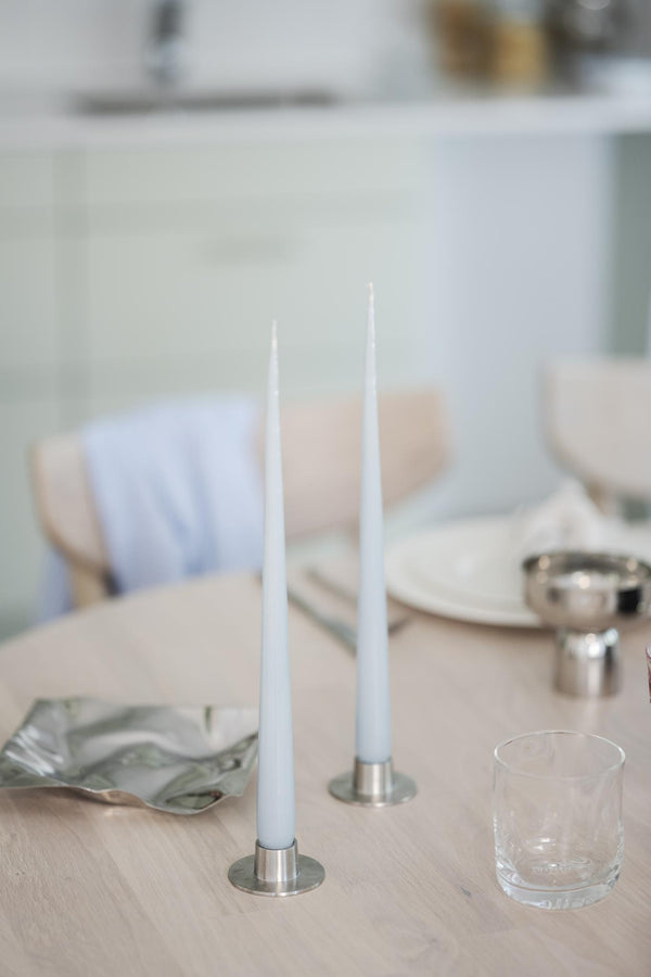 Ljusblå taper-ljus i silverfärgade ljusstakar på dukat bord med glas och tallrikar i pastellfärger