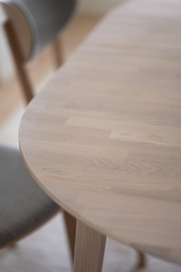 Rund bordsskiva i ljust trä med synlig ådringsmönster och träben i skandinavisk design