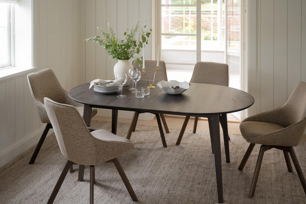 Runt matbord i mörkt trä med fyra beige stoppade stolar i modern skandinavisk matsal