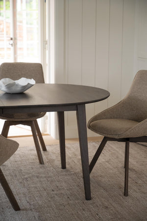 Runt matbord i mörkt trä med grå stoppad matstol i modern skandinavisk design