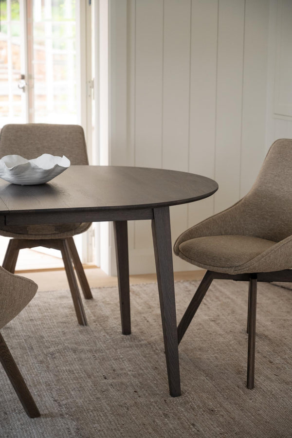 Runt matbord i mörkt trä med grå stoppad matstol i modern skandinavisk design