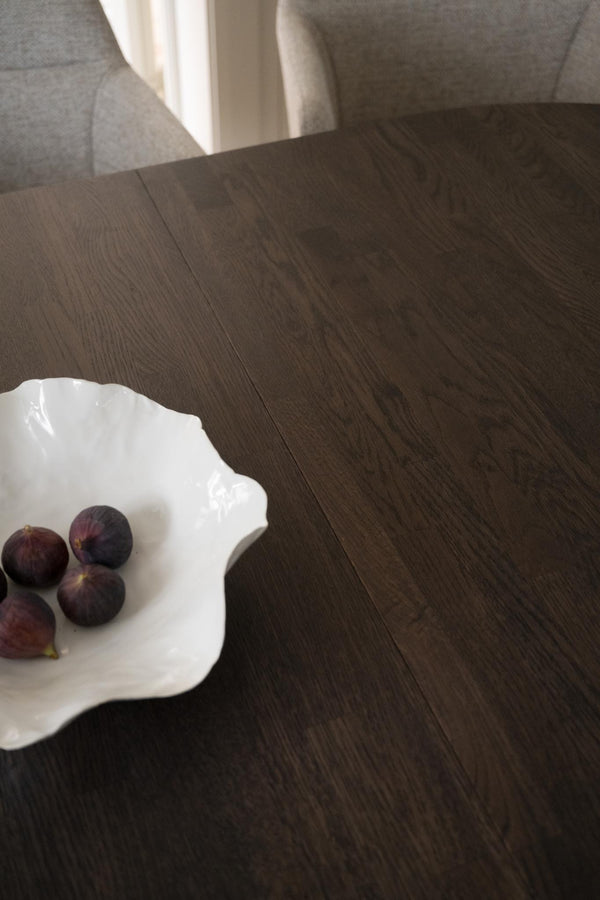 Mörkbrun parkettgolv i ek med synlig trästruktur, vit dekorativ tallrik med fikon på soffbord