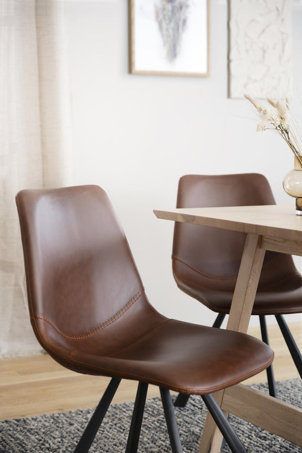 Bruna läder matstolar med svarta ben vid ljust trä matbord i modern skandinavisk matsal