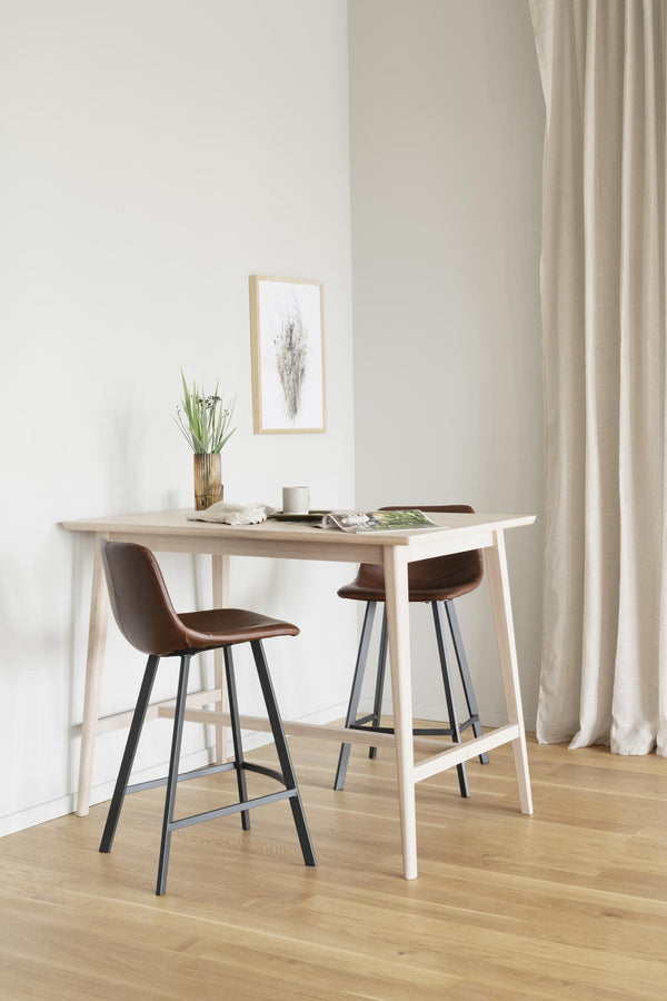 Ljust matbord i trä med två bruna barstolar, dekorerat med vas och tavla i minimalistisk skandinavisk stil