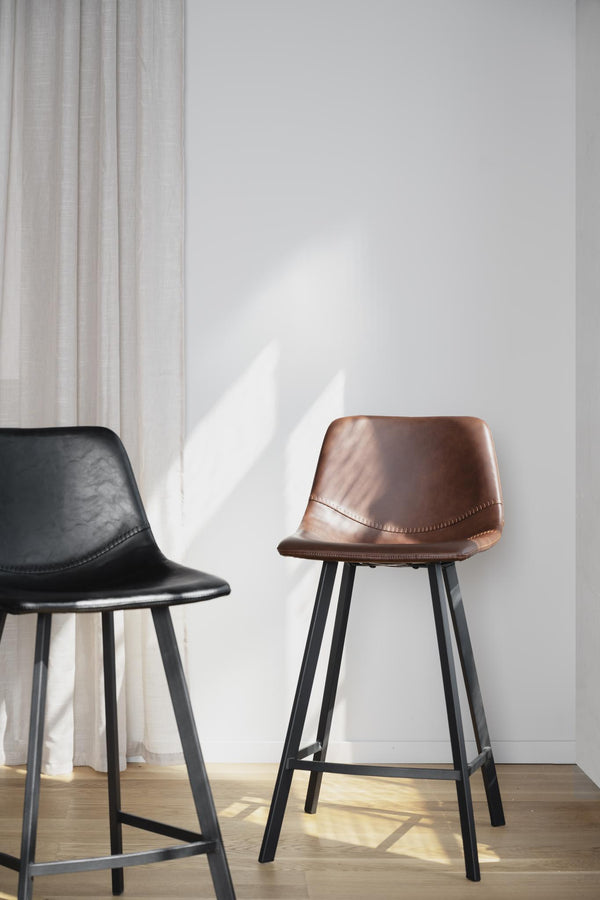 Barstolar i svart och brunt läder med metallben mot vit vägg med skuggspel från fönster