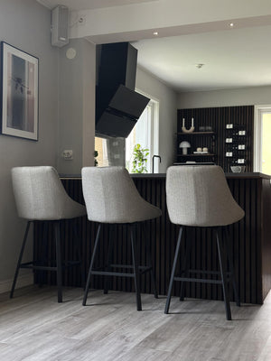 Tre ljusgrå barstolar med svarta ben vid köksö med räfflad svart front i modernt kök