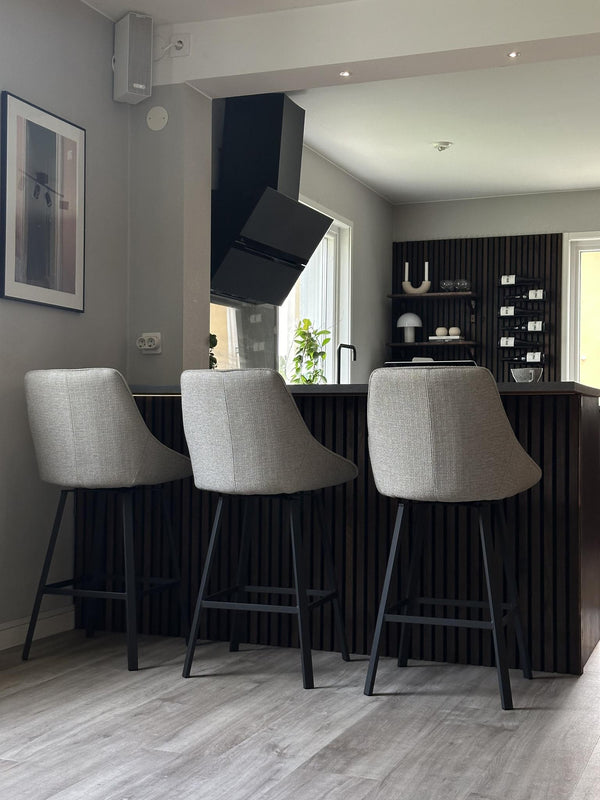 Tre ljusgrå barstolar med svarta ben vid köksö med räfflad svart front i modernt kök