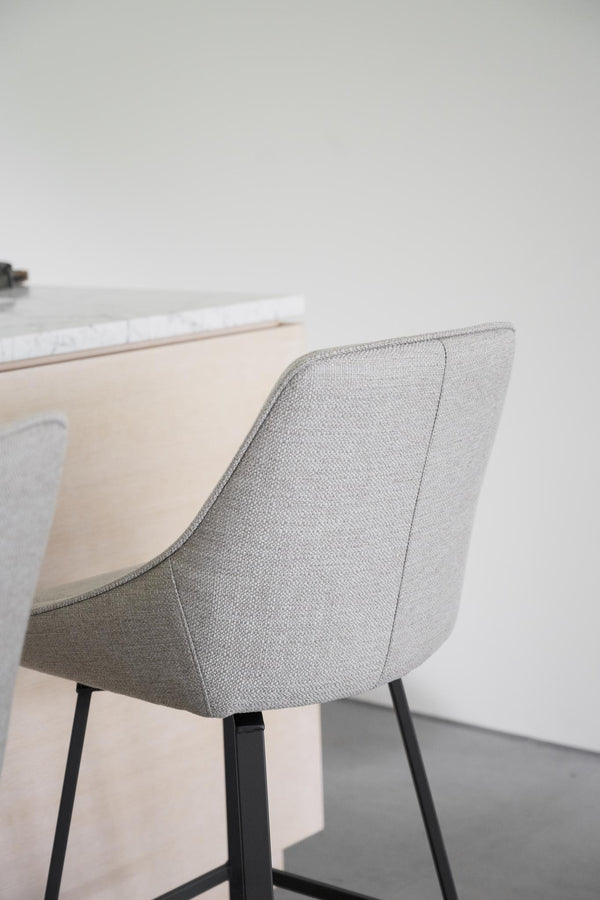 Grå stoppad matstol med svarta ben vid ljust trädining bord i minimalistisk skandinavisk stil