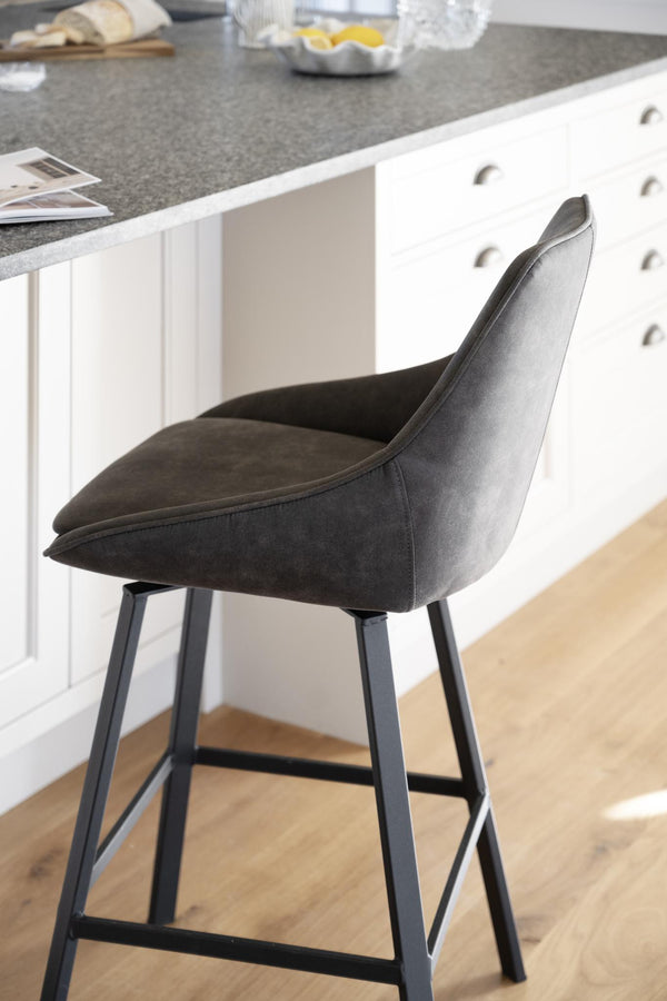 Grå sammetsklädd barstol med svarta metallben vid vitt köksbord med grå bänkskiva