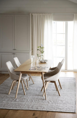 Matbord i ljust trä med fyra vita stolar på grå matta i ljust matrum med skåp