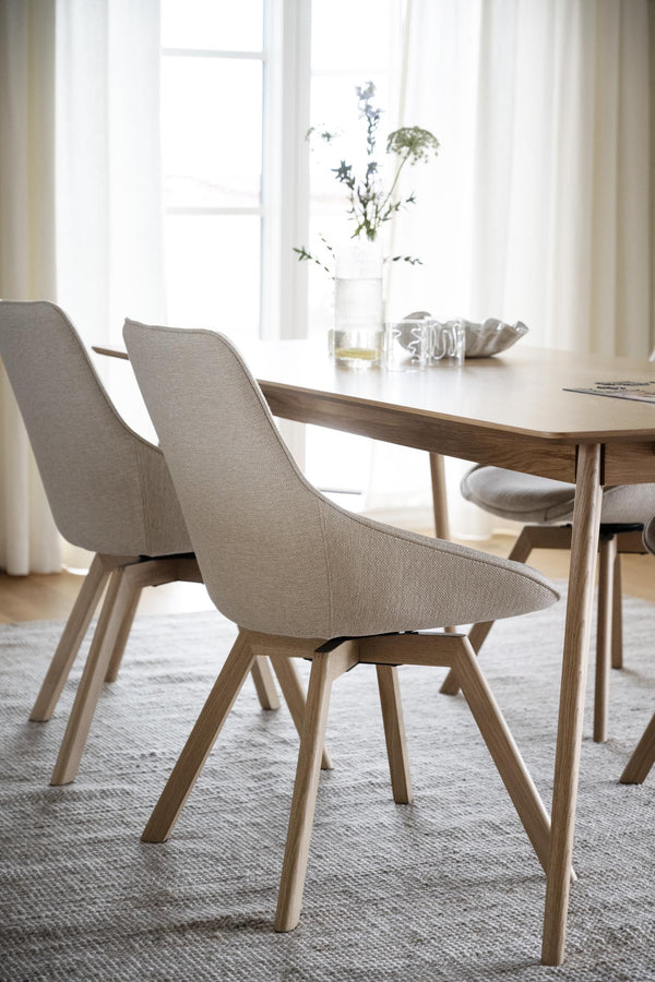 Matbord i ek med beige stoppade stolar i skandinavisk design med träben