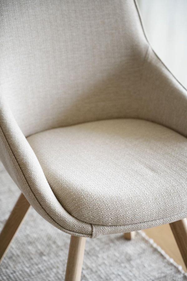 Beige stol med stoppad sits och rygg i linnelikt tyg på ljusa träben